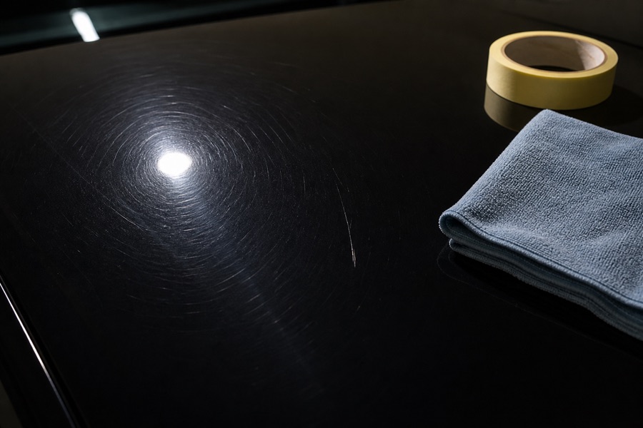 Close inspection of car paint showing light swirls, a deeper scratch and a clean reference area